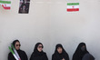 Veiled Iranian women sit under a poster depicting portraits of Iran's late and new Supreme...