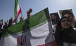 A young demonstrator holding a national flag stands under portraits of Iran's Supreme Lead...