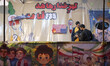 Two pro-government supporters stand together at a play stand covered with banners depictin...