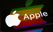 The Apple logo is displayed on a smartphone screen placed on a reflective surface onto whi...