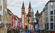 Pedestrians fill the shopping street with tram tracks and retail storefronts leading towar...