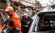 An injured man with a bandaged head stands on the rubble of a building destroyed in the Kh...