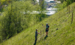 Workers install fence posts and perform spring maintenance on a steep alpine meadow slope...