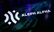 The Aleph Alpha logo is displayed on a smartphone screen placed on a reflective surface on...