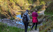 Two hikers walk beside a rocky stream on a forest trail in Berchtesgaden, Upper Bavaria, B...