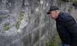 An elderly man looks through holes in the fence of a cemetery in the Solomianskyi district...