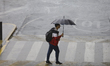 A person shields themselves from the rain with an umbrella during a yellow alert for rain...