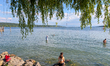 People sit on rocks and stand in the water at Lake Starnberg in Starnberg, Upper Bavaria,...