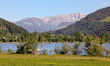 People with sun umbrellas relax by Lake Grosser Alpsee with the Allgaeu Alps in the backgr...
