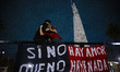 A mother and her son embrace atop a fence with a flag bearing the lyrics of an Indio Solar...