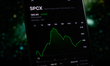 The SpaceX stock price is displayed on a smartphone screen with a space-themed illustratio...