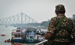 A security personnel stands guard along the Hooghly River as boats and ferries operate on...