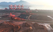 Large machinery piles up inventory of imported iron ore just unloaded from a cargo ship at...