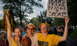 Three people dressed in support of trans athletes hold themed items during the beginning o...