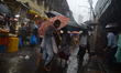 Commuters and vendors walk with umbrellas through a rain-soaked market street as monsoon s...