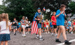 Members of a marching band play instruments while walking down a street during the 4th of...