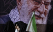 Veiled Iranian women stand in front of a portrait of Iran's late Supreme Leader Ayatollah...