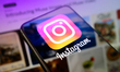 The Instagram logo is displayed on a smartphone screen placed on a reflective surface onto...
