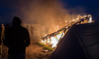 Migrants stand in the Calais Jungle in front of a hut which is set on fire  in Calais, Fra...
