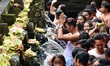 A man pray between people who wait in queue to get the holy water from fountains in Tirta...