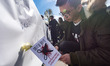 People hold symbolic scissor props and flowers during a gathering at Place de la Republiqu...