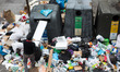 A man throws a cardboard box in a recycle container surrounded by trash during the fourth...