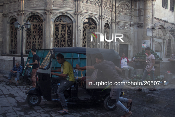 Two young egyptians are pushing a Tuk Tuk to make it start in Old Cairo on June 15, 2017 
