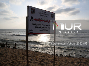 A warning sign reading 'dangerous swimming and fishing' is placed near an outlet flowing sewage into the sea in front in the Shati refugee c...