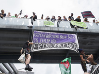 People hanging from a bridge and carrying a banner reading 'G20 wir are not all. The drowned are missing' attend a protest march against the...