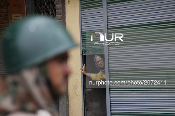 A kashmiri Women peeps out from an half closed shop shutter as an Indian paramilitary stands guard during a curfew  in old city Srinagar  on...