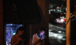 Two women are seen using their mobile phones while taking cover from the rain near an ATM...