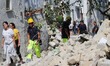 Rescuers teams walk near a damaged building in one of the more heavily damaged areas on Au...