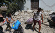 People walk near a house, destroyed in the earthquake in one of the more heavily damaged a...