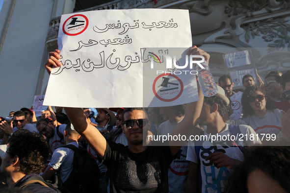 A protester raises a placard that reads in Arabic "Tunisian people are free, and the economic reconciliation bill will not pass" as he atten...