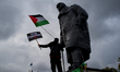 A pro-Palestine demonstrator waves Palestine flag and holds a placard on the statue of Sir...
