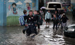 A Palestinian man carrying students walk in a street flooded by rain water, in Gaza city o...