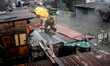 A resident carries a dog as he makes his way along rooftops to escape rising floodwaters i...