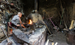 Iranian elderly man works by a stove in his blacksmith workshop in historical bazaar in Ya...