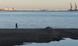 A man walks on the Spanish cost line in Melilla, with a background view of Nador Port.On...