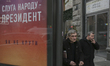 Two men walk past a political advertisement of Oleksandr Zelenskyi which says "President i...