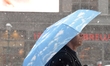 A man holding a blue sky umbrella walks on Market Street as commuters get an early jump on...