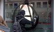 Mlitant with hood tagging a bank with the circle-A anarchist symbol during an antifascist...