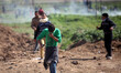 A Palestinian demonstrator throws back a tear gas canister as others run from gas fired by...