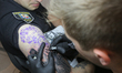 Master tattoos a man dressed in police uniform during the tattoo festival in Kyiv, Ukraine...