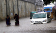 Commuters and other local residents are seen in the rain loging water after a heavy rain f...