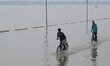 Indian boys ride their bicycles in partially submerged road , on the flooded banks of Gang...