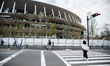 People are seen walking past the building of the Olympic Stadium of Tokyo, who will host t...