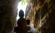 A statue of a small Buddha inside of Phnom Kampong Tranch.  The roof of a large cave in t...