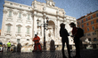 A worker and a couple of tourists with protective masks near the Trevi Fountain closed to...