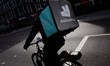 A Deliveroo courier cyclist waits at traffic lights on a near-deserted Tottenham Court Roa...